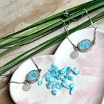 Verstellbares Edelstahlarmband mit Zirkoniasteinchen und Schiebeverschluss und rundem Anhänger (ca. 2,5 × 1,7 cm) mit echten Larimar-Edelstein-Splittern in Harz. Zusätzlich ein Charm „Blume des Lebens“ aus 925 Silber. Handgefertigtes Unikat in Türkis- und Meeresblautönen – Schmuckstück in Nahaufnahme bzw. als Tragebild am Handgelenk.