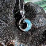 Feine Wellen-Kette aus rhodiniertem 925 Silber. Der runde Anhänger zeigt eine stilisierte Welle mit hellblauem Larimar-Cabochon, eingefasst in poliertem Silber. Größe des Anhängers ca. 23 x 13 mm, an einer 45 cm langen, 1 mm starken, rhodinierten Silberkette. 