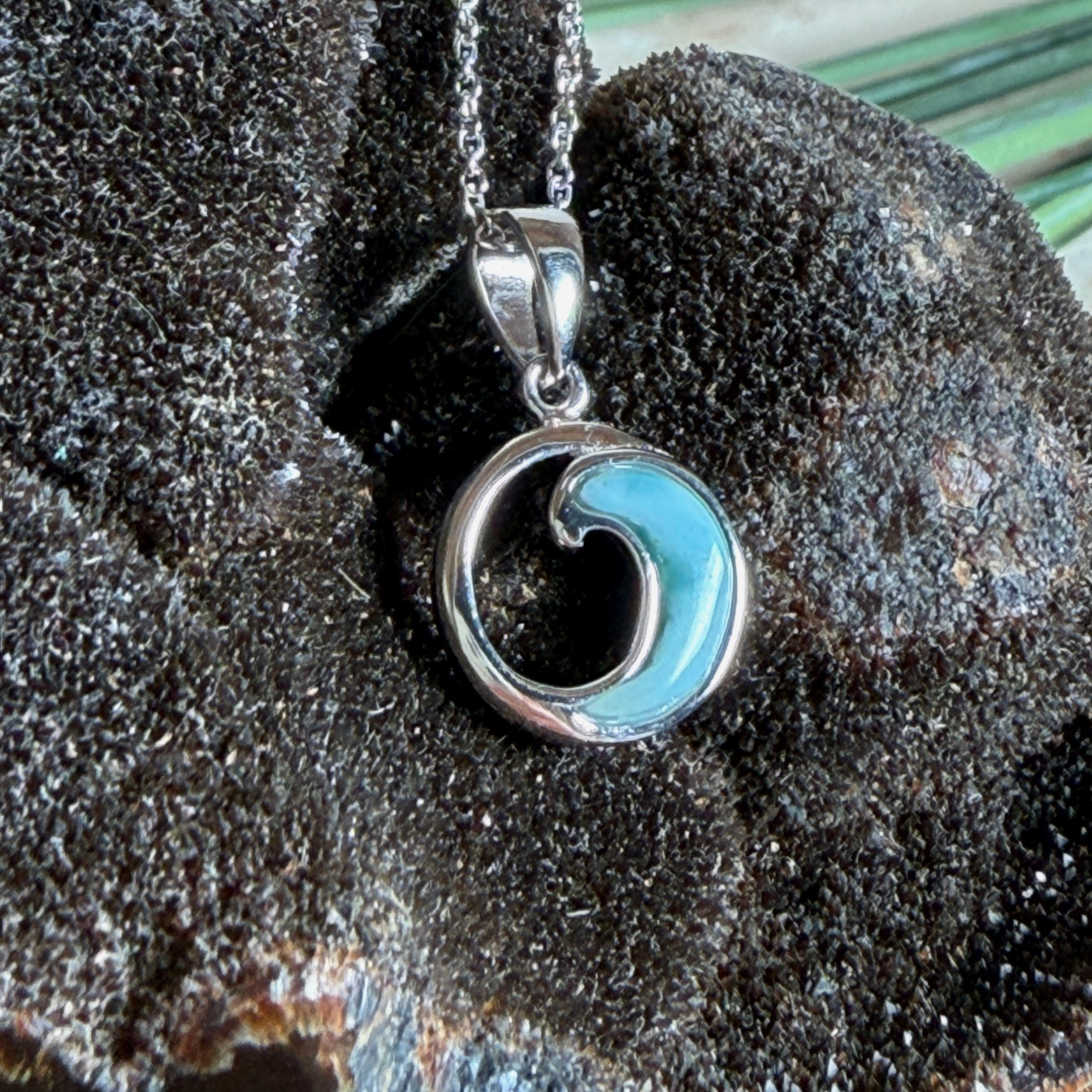 Feine Wellen-Kette aus rhodiniertem 925 Silber. Der runde Anhänger zeigt eine stilisierte Welle mit hellblauem Larimar-Cabochon, eingefasst in poliertem Silber. Größe des Anhängers ca. 23 x 13 mm, an einer 45 cm langen, 1 mm starken, rhodinierten Silberkette. 