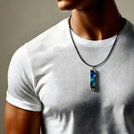 Rechteckiger Stabanhänger aus Maserholz und glasklarem Epoxidharz in tiefen Blau- und Türkistönen mit organischer Lagunen/Riff-Optik. Hochglanzpoliert, ca. 4,6 × 1,2 cm. Der Anhänger hängt an einer schwarzen Lederkette mit Edelstahl-Karabiner und 5-cm-Verlängerung (45 + 5 cm); die Anhängerschlaufe ist ebenfalls aus Edelstahl. Handgefertigtes Unikat, Lieferung in edler Schmuckbox – maritimer Look.