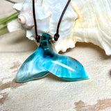 Walflossen-Anhänger „Flossenklang“ – handgefertigtes Unikat aus Maserholz und türkis-blau-grauen und weißem Harz. Die elegant geschwungene Form erinnert an die Flosse eines Wals und symbolisiert Freiheit, Stärke und Naturverbundenheit. Mit verstellbarem braunem Lederband gefertigt, ist jedes Stück ein individuelles Schmuckstück für Meeresliebhaber und Natursuchende. Maritimer Halsschmuck, inspiriert vom Ozean, glatt poliert und mit Liebe zum Detail von Hand gearbeitet.