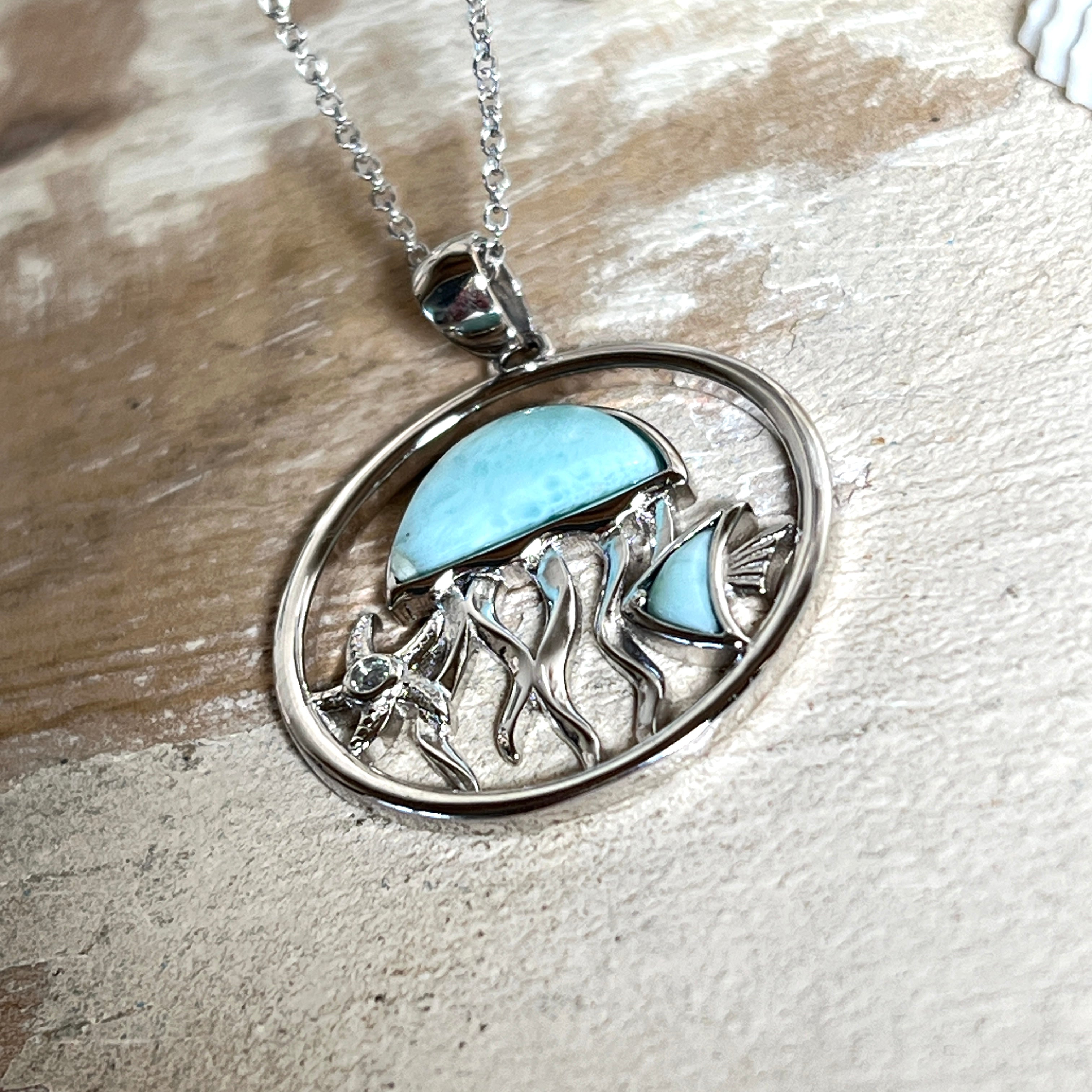 „Sealife“ – runder Anhänger aus rhodiniertem 925 Sterling Silber mit seltenem Larimar und funkelndem Topas. Das maritime Design zeigt eine Qualle, einen Fisch und einen Seestern. Anhängergröße ca. 32 × 26 mm, inklusive 45 cm langer Silberkette (1 mm Stärke). Symbol für die Schönheit und Vielfalt des Ozeans – jedes Stück ein Unikat durch das natürliche Farbspiel des Larimars.