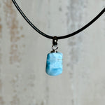 Larimar Freeform Anhänger mit rhodinierter Silberöse an schwarzer Lederkette. Der seltene, kostbare Larimar („Atlantisstein“) zeigt ein lebendiges Muster aus Türkis- und Weißtönen. Beidseitig tragbar, Steingröße ca. 2 x 1 cm, Lederkette 45 cm mit Edelstahl-Karabiner und 5 cm Verlängerung. Natürlicher, maritimer Unikatschmuck.