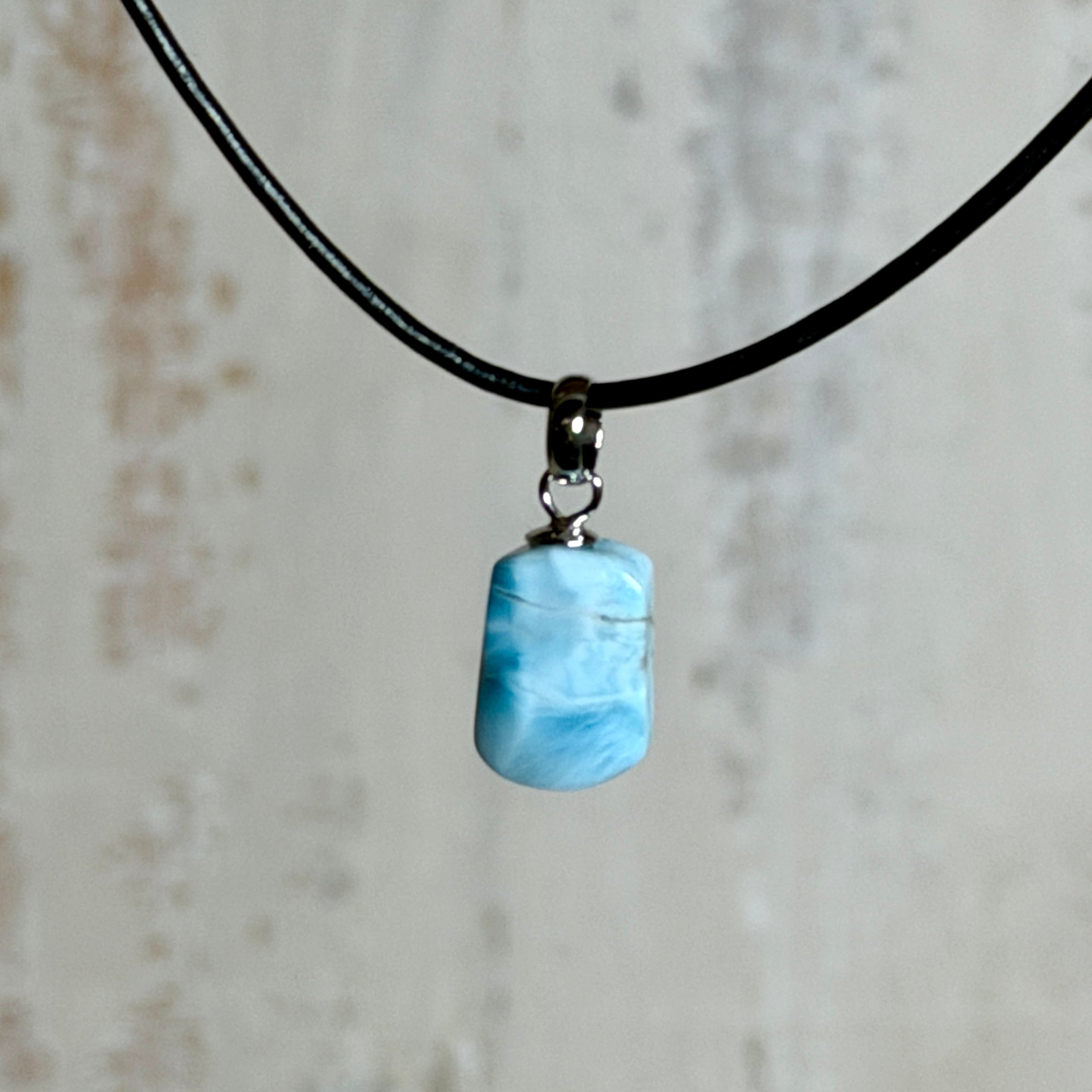 Larimar Freeform Anhänger mit rhodinierter Silberöse an schwarzer Lederkette. Der seltene, kostbare Larimar („Atlantisstein“) zeigt ein lebendiges Muster aus Türkis- und Weißtönen. Beidseitig tragbar, Steingröße ca. 2 x 1 cm, Lederkette 45 cm mit Edelstahl-Karabiner und 5 cm Verlängerung. Natürlicher, maritimer Unikatschmuck.