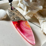 Aurora Flame – fluoreszierender Surfbrett-Anhänger aus Maserholz und leuchtendem Epoxidharz in Rosa, Pink, Orange und Weiß. Der handgefertigte Unikat-Anhänger fluoresziert bei Schwarzlicht in intensiven Farbtönen. Er ist ca. 6,3 x 2 cm groß, wird an einem verstellbaren Lederband (26–45 cm) getragen und ist mit einer silberfarbenen Spacerperle verziert. Ein ausdrucksstarkes Schmuckstück für Menschen mit Persönlichkeit.