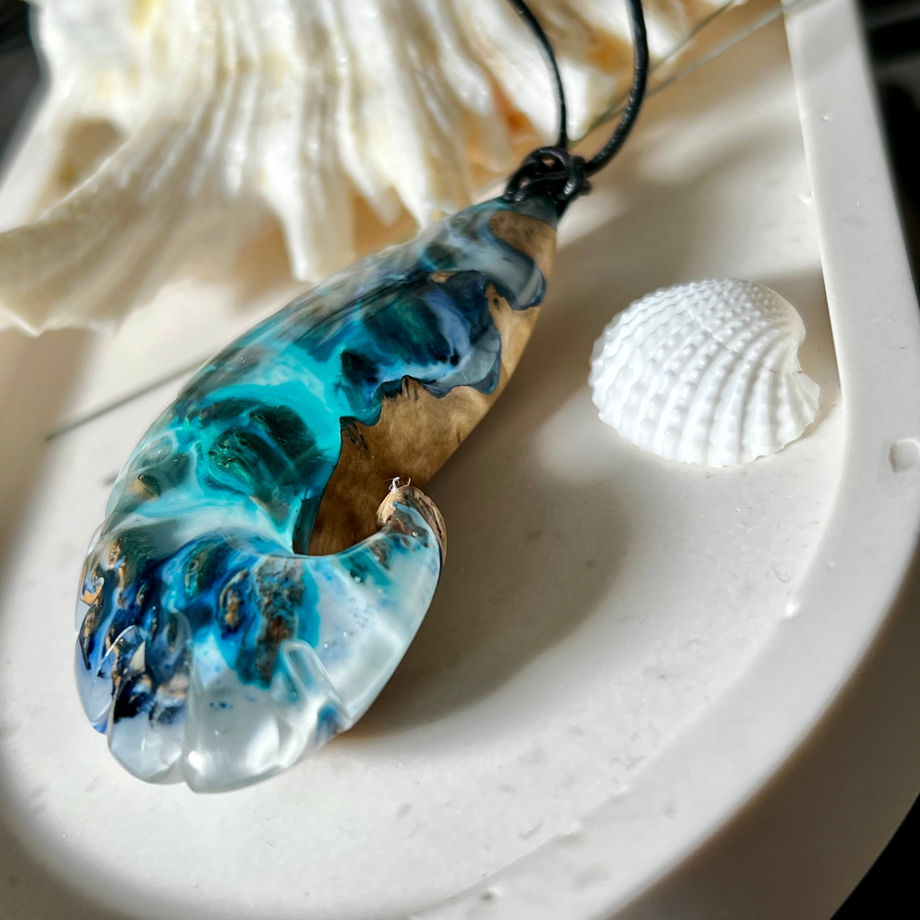 Ocean Nautilus Halskette – handgefertigter Anhänger aus  Epoxidharz und edlem Maserholz in kräftigem Blau, Türkis und Weiß, geformt wie eine stilisierte Nautilus-Muschel. Die einzigartige Maserung des Holzes trifft auf transparente Tiefenwirkung des Harzes. Der ca. 7 cm große Anhänger hängt an einem verstellbaren Lederband mit dekorativen Holzperlen (26–48 cm). Jedes Stück ist ein maritimes Unikat, inspiriert von der Magie des Meeres.