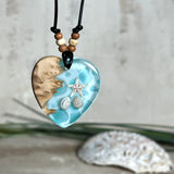 Handgefertigter Herzanhänger aus Maserholz und transparentem Ocean-Harz mit echtem Seestern und Muscheln. Die zarten Aqua-Farben erinnern an Meereswellen. Lederband verstellbar mit Holzperlen. Größe ca. 3,5 × 3,2 cm. Natürliches, maritimes Unikat von ZeitlosSchmuckDesign