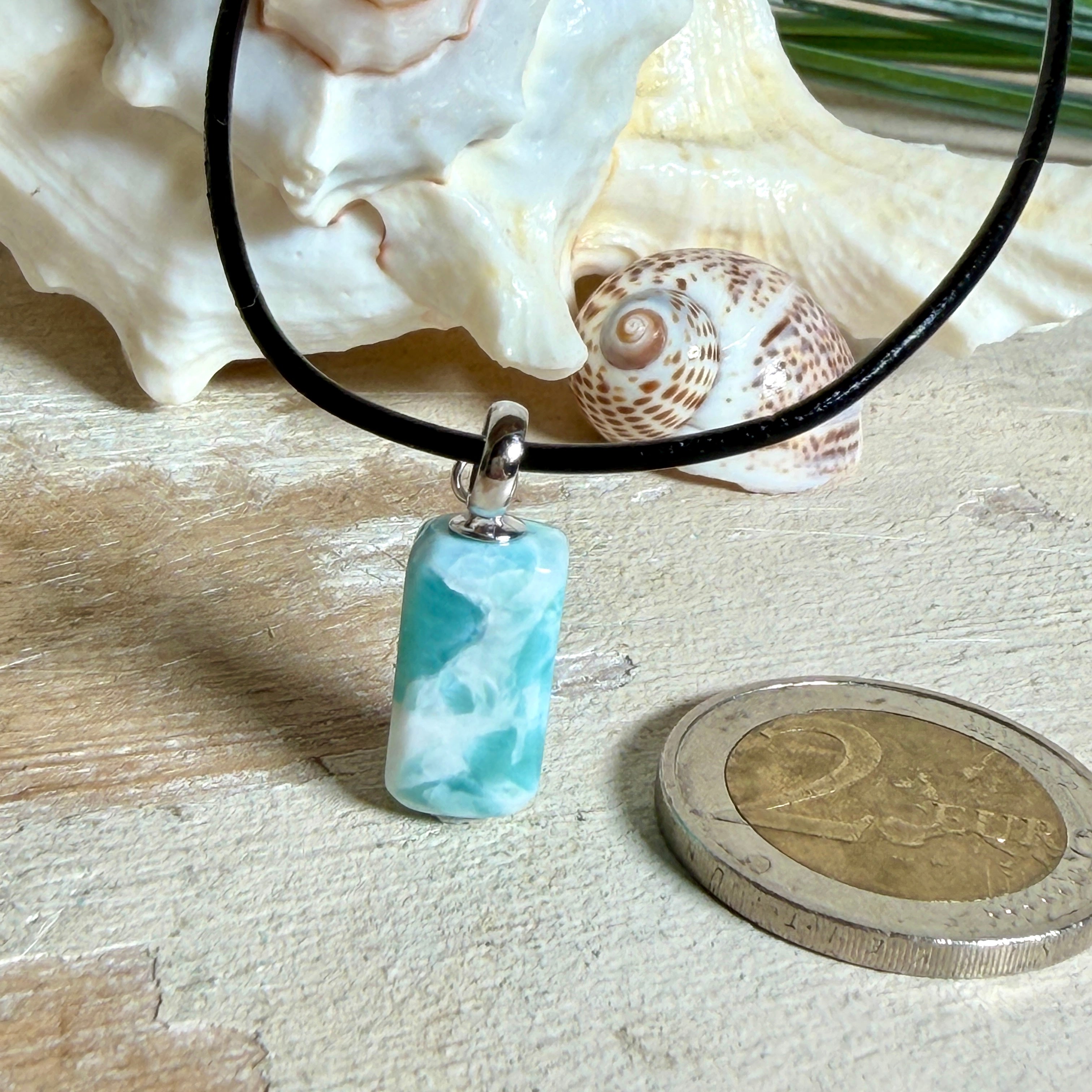Larimar Freeform Anhänger an schwarzer Lederkette. Natürlicher, rechteckiger Larimar-Stein (ca. 1,5 × 1 cm) in Türkis-Blau mit weißen Strukturen, eingefasst in eine rhodinierte Silberöse. Beidseitig tragbar, an 45 cm Lederkette mit Edelstahl-Karabinerverschluss und 5 cm Verlängerung. Maritimes, zurückhaltend elegantes Schmuckstück mit der Optik karibischen Meerwassers.