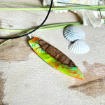 Handgefertigte Halskette „Tropical Glow“ mit Surfbrett-Anhänger aus naturbelassenem Rebholz (Weinrebe) und marmoriertem Epoxidharz in Grün, Orange, Türkis und Weiß. Größe des Anhängers ca. 6,5 × 2 cm. Das Harz fluoresziert eindrucksvoll unter UV-/Schwarzlicht. Edelstahl-Anhängerschlaufe, schwarze Lederkette (45 cm + 5 cm Verlängerung) mit Edelstahl-Karabiner. Unikat in maritim-sommerlichem Stil, ideal als besonderes Geschenk.