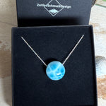 Feine Kette mit rundem Larimar-Cabochon in AA-Qualität. Der ca. 20 mm große Stein zeigt ein intensives Blau mit hellen, netzartigen Zeichnungen und ist mittig mit einer 2,5 mm Bohrung versehen, durch die eine zarte 925 Silberkette (45 cm, ca. 1 mm stark) geführt wird. 