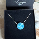 Feine Kette mit rundem Larimar-Cabochon in AA-Qualität. Der ca. 20 mm große Stein zeigt ein intensives Blau mit hellen, netzartigen Zeichnungen und ist mittig mit einer 2,5 mm Bohrung versehen, durch die eine zarte 925 Silberkette (45 cm, ca. 1 mm stark) geführt wird. 