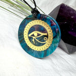 Runder Anhänger mit goldenem Horusauge aus Metall in blau türkis violettem Epoxidharz am schwarzen Baumwollband, spiritueller Eye of Ra Naturschmuck Amulett