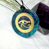 Runder Anhänger mit goldenem Horusauge aus Metall in blau türkis violettem Epoxidharz am schwarzen Baumwollband, spiritueller Eye of Ra Naturschmuck Amulett