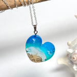 Ein herzförmiger Anhänger mit einer ganzen Ozeanwelt darin: Welle, Sand und Seestern in leuchtendem Blau und Türkis – handgegossen, einzigartig, unvergesslich. Mit versilberter Kette (46 cm) und Edelstahl-Karabiner.
