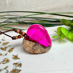 Handgefertigter Herzanhänger aus Olivenholz und leuchtend pinkem Epoxidharz mit eingeschlossenen Pusteblumensamen. Verstellbares braunes Lederband mit Holzperlen, Anhänger ca. 3,5 × 3,3 cm groß. Das Harz leuchtet dezent unter Schwarzlicht. Ein einzigartiges Unikat von ZeitlosSchmuckDesign, inspiriert von Kindheitsglück und Pusteblumen.