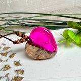 Handgefertigter Herzanhänger aus Olivenholz und leuchtend pinkem Epoxidharz mit eingeschlossenen Pusteblumensamen. Verstellbares braunes Lederband mit Holzperlen, Anhänger ca. 3,5 × 3,3 cm groß. Das Harz leuchtet dezent unter Schwarzlicht. Ein einzigartiges Unikat von ZeitlosSchmuckDesign, inspiriert von Kindheitsglück und Pusteblumen.