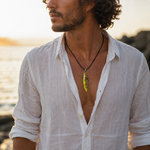 KI-Tragebild eines Mannes mit handgefertigter Halskette „Tropical Glow“ – Surfbrett Anhänger aus Rebholz und fluoreszierendem Epoxidharz in Grün, Orange und Türkis an schwarzem Lederband, maritimer Unisex Schmuck im Strandlook.