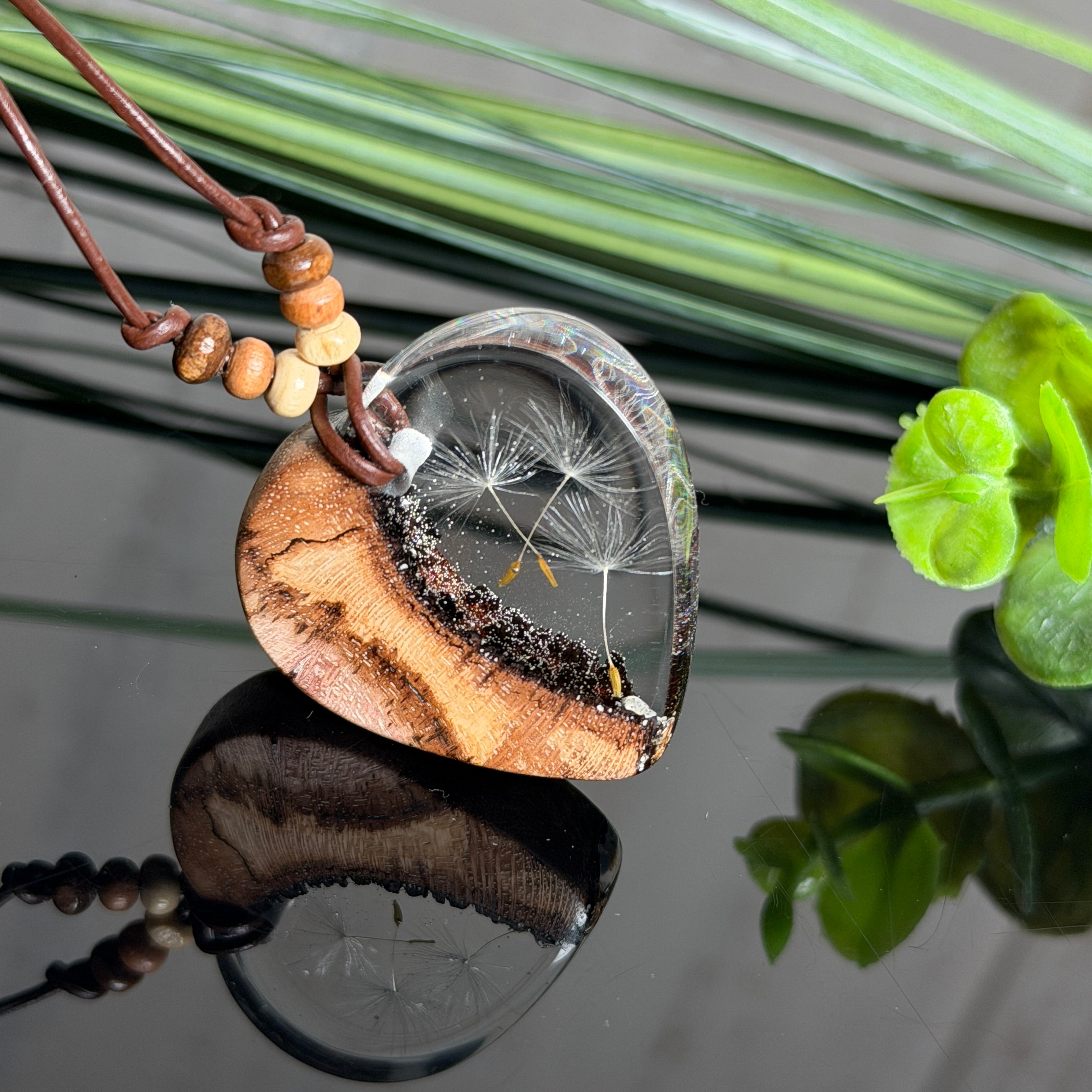 Herzanhänger „Pusteblumenzauber“ aus naturbelassenem Rebholz und klarem Epoxidharz mit schwebenden Pusteblumensamen. Dunkelbraunes, verstellbares Lederband mit kleinen Holzperlen, Anhänger ca. 3,5 × 3,5 cm. Handgefertigtes Unikat von ZeitlosSchmuckDesign.