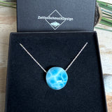 Feine Kette mit rundem Larimar-Cabochon in AA-Qualität. Der ca. 20 mm große Stein zeigt ein intensives Blau mit hellen, netzartigen Zeichnungen und ist mittig mit einer 2,5 mm Bohrung versehen, durch die eine zarte 925 Silberkette (45 cm, ca. 1 mm stark) geführt wird. 