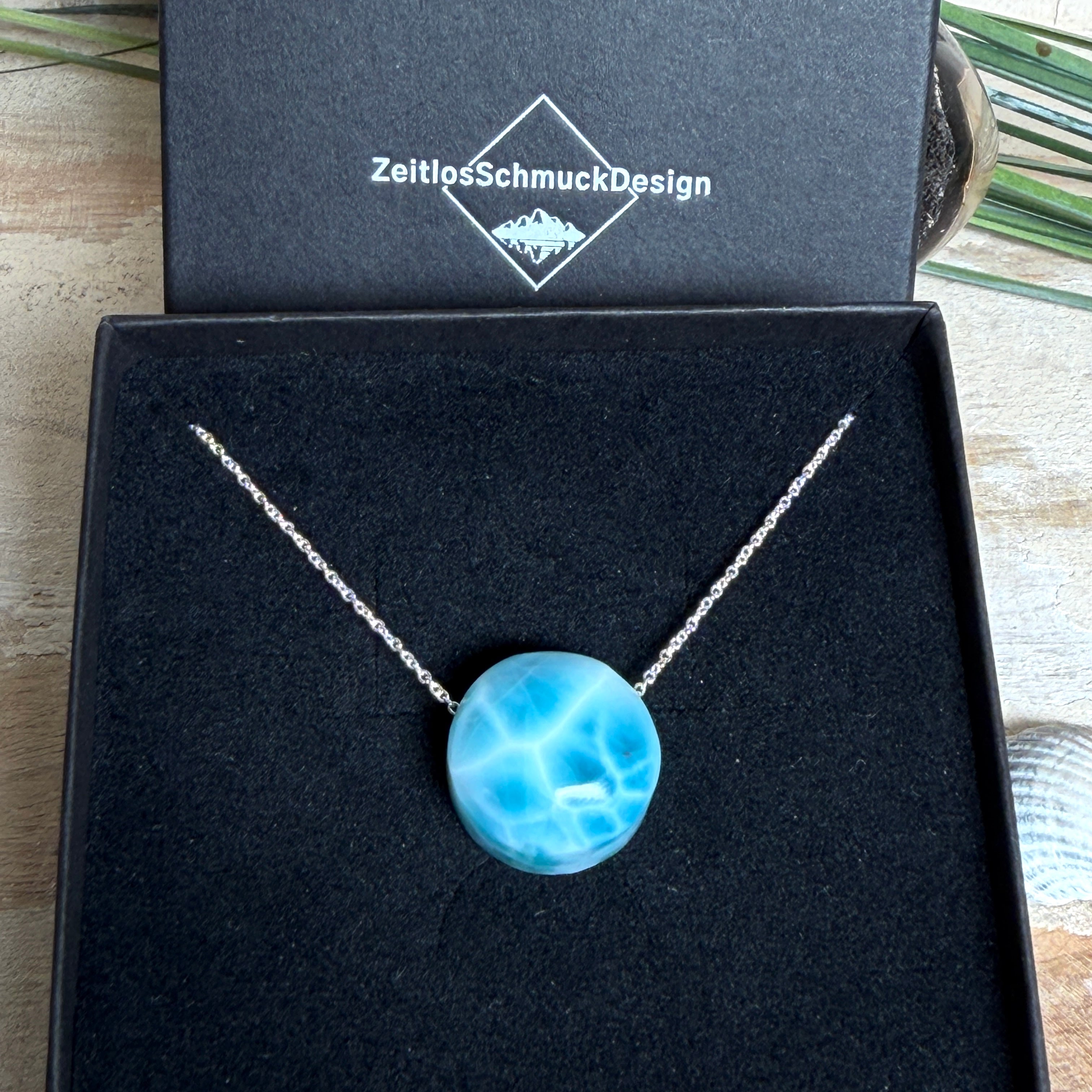 Feine Kette mit rundem Larimar-Cabochon in AA-Qualität. Der ca. 20 mm große Stein zeigt ein intensives Blau mit hellen, netzartigen Zeichnungen und ist mittig mit einer 2,5 mm Bohrung versehen, durch die eine zarte 925 Silberkette (45 cm, ca. 1 mm stark) geführt wird. 