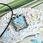 Quadratischer Larimar-Mosaik Anhänger im Edelstahlrahmen mit Seestern-Element und facettierter Bergkristall-Perle, eingebettet in Harz, an schwarzer Lederkette.