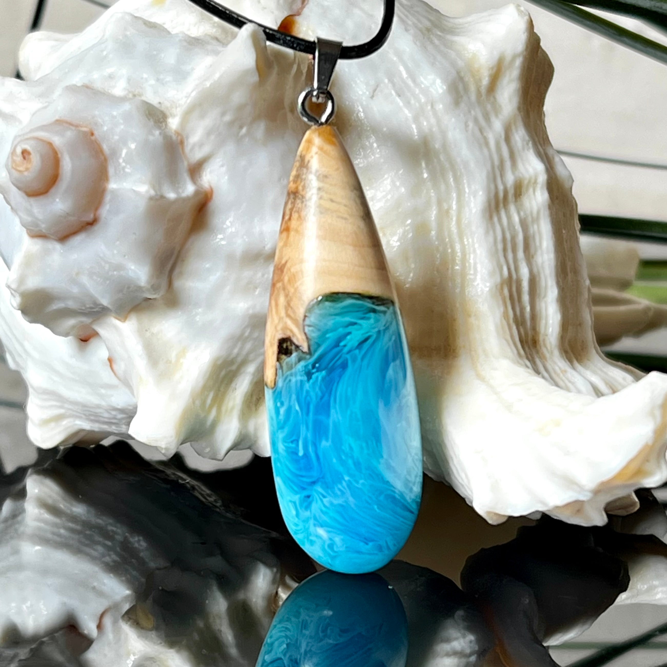 Tropfenförmiger Anhänger aus Maserholz und Harz in leuchtenden Blautönen und Weiß. Inspiriert vom Meer, in Handarbeit gegossen,gesägt, geschliffen und hochglanzpoliert. Mit verstellbarer Lederkette (45 + 5 cm) und Edelstahlkarabiner. Jeder Anhänger ist ein Unikat mit natürlicher Maserung. Ein maritimes Schmuckstück für Naturfreunde und alle, die das Wasser lieben.