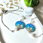 Elegantes Edelstahl-Armband mit rundem Resin-Anhänger in Meeresblau. Im Anhänger liegt echter Meersand als Ufersaum; darüber Sticker-Motive Seestern & Muschel. Zwei feine Süßwasserperlen verzieren das Armband. Verstellbarer Schiebeverschluss . Handgefertigtes Unikat – maritimer Schmuck, der an Wellenrauschen und Strandspaziergänge erinnert.