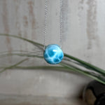 Feine Kette mit rundem Larimar-Cabochon in AA-Qualität. Der ca. 20 mm große Stein zeigt ein intensives Blau mit hellen, netzartigen Zeichnungen und ist mittig mit einer 2,5 mm Bohrung versehen, durch die eine zarte 925 Silberkette (45 cm, ca. 1 mm stark) geführt wird. 