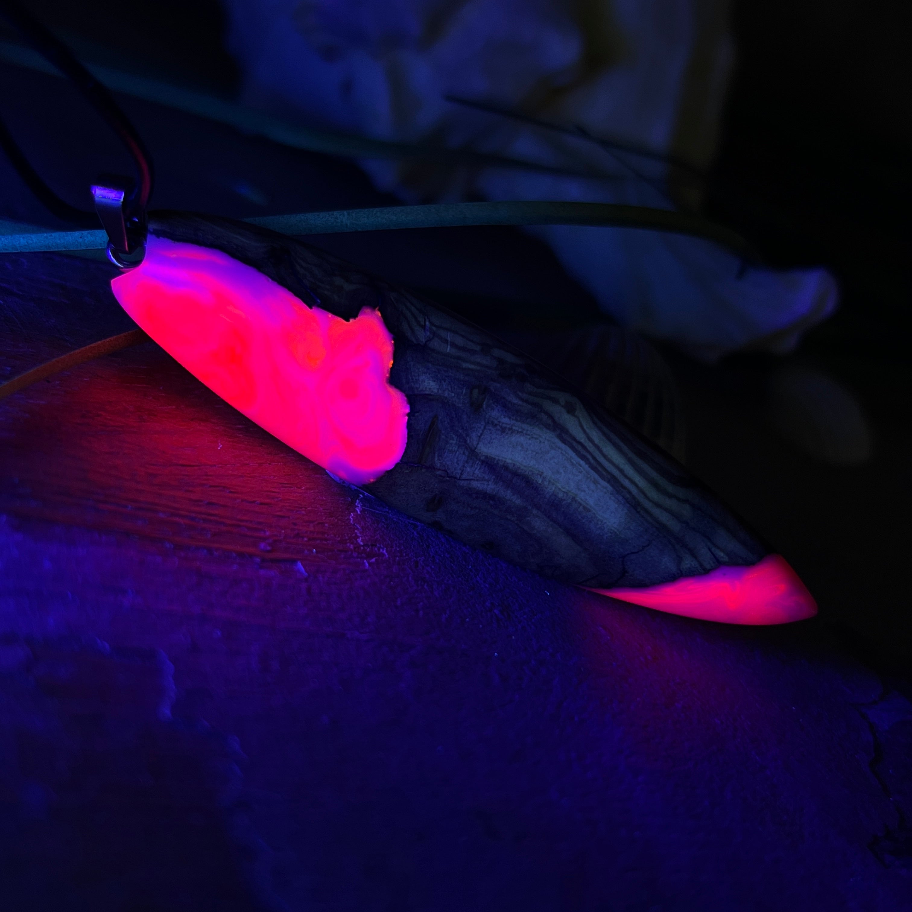 Handgefertigter Surfbrett-Anhänger „Pink Glow“ aus edlem Olivenholz und fluoreszierendem Epoxidharz in Pink & Weiß. Fluoreszierend bei Schwarzlicht, mit Edelstahl-Anhängerschlaufe und schwarzer Lederkette (45 cm + 5 cm Verlängerung). Ein maritimes Unikat – perfekt als Geschenk für Surfer und Meeresliebhaber.