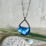 „Lagunenlicht“ – Tropfenanhänger mit handmodellierter 3D-Welle und feinem Glitzereffekt. Klarer Harzlook in Blau/Türkis, gefasst in Silber-Legierung. Größe ca. 3,5 × 2 cm. Geliefert an einer versilberten Kette (ca. 56 cm). Hochglänzend , maritimer Unikatcharakter.