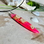 Handgefertigter Surfbrett-Anhänger „Flame Surf“ aus Maserholz und fluoreszierendem Harz in kräftigem Pink. Das Schmuckstück leuchtet bei Schwarzlicht und wird an einer schwarzen Lederkette mit Edelstahl-Karabiner (45 cm + 5 cm Verlängerung) geliefert. Größe ca. 6,7 × 2 cm. Ein Unikat für Surf- und Strandliebhaber, edel verarbeitet und mit Liebe gefertigt.