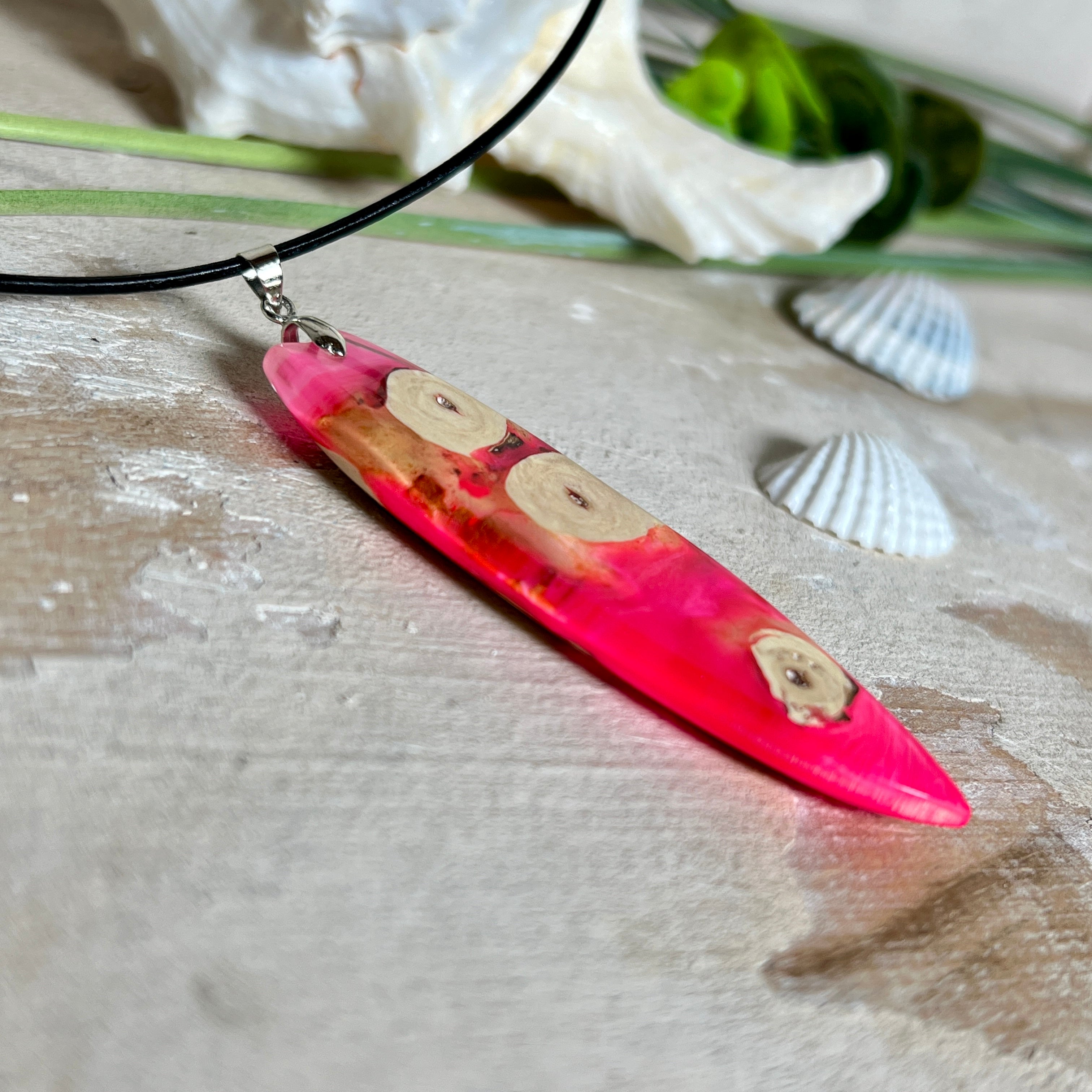 Handgefertigter Surfbrett-Anhänger „Flame Surf“ aus Maserholz und fluoreszierendem Harz in kräftigem Pink. Das Schmuckstück leuchtet bei Schwarzlicht und wird an einer schwarzen Lederkette mit Edelstahl-Karabiner (45 cm + 5 cm Verlängerung) geliefert. Größe ca. 6,7 × 2 cm. Ein Unikat für Surf- und Strandliebhaber, edel verarbeitet und mit Liebe gefertigt.