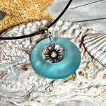 Handgefertigte Halskette mit Donut-Anhänger aus türkisfarbenem Seeglas, kombiniert mit einem filigranen Sonnen-Charm aus Edelstahl. Die Kette besteht aus einer schwarzen Lederschnur (1,5 mm) mit Karabiner und Verlängerungskette aus Edelstahl. Maritimes Schmuckstück für Meerliebhaberinnen und Sommerfreunde. Unikat mit stilvoller Ausstrahlung.