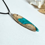 Handgefertigte Surfbrett Kette aus Maserholz und türkisfarbenem Resin mit Edelstahl Anhängerschlaufe an schwarzer Lederkette mit Karabiner und Verlängerung. Filigraner Ocean Anhänger inspiriert von Meer und Wellen, natürlicher Unikat Schmuck für Damen und Herren.