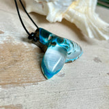 Handgefertigter Walflossen-Anhänger „Flossenklang“ aus Maserholz und türkis-blau-grau-weiß marmoriertem Epoxidharz an verstellbarem Lederband. Maritime Kette als Unikatschmuck für Meeresliebhaber und Wal-Fans, hochwertig poliert, präsentiert vor Muscheldeko und in Schmuckbox von ZeitlosSchmuckDesign.