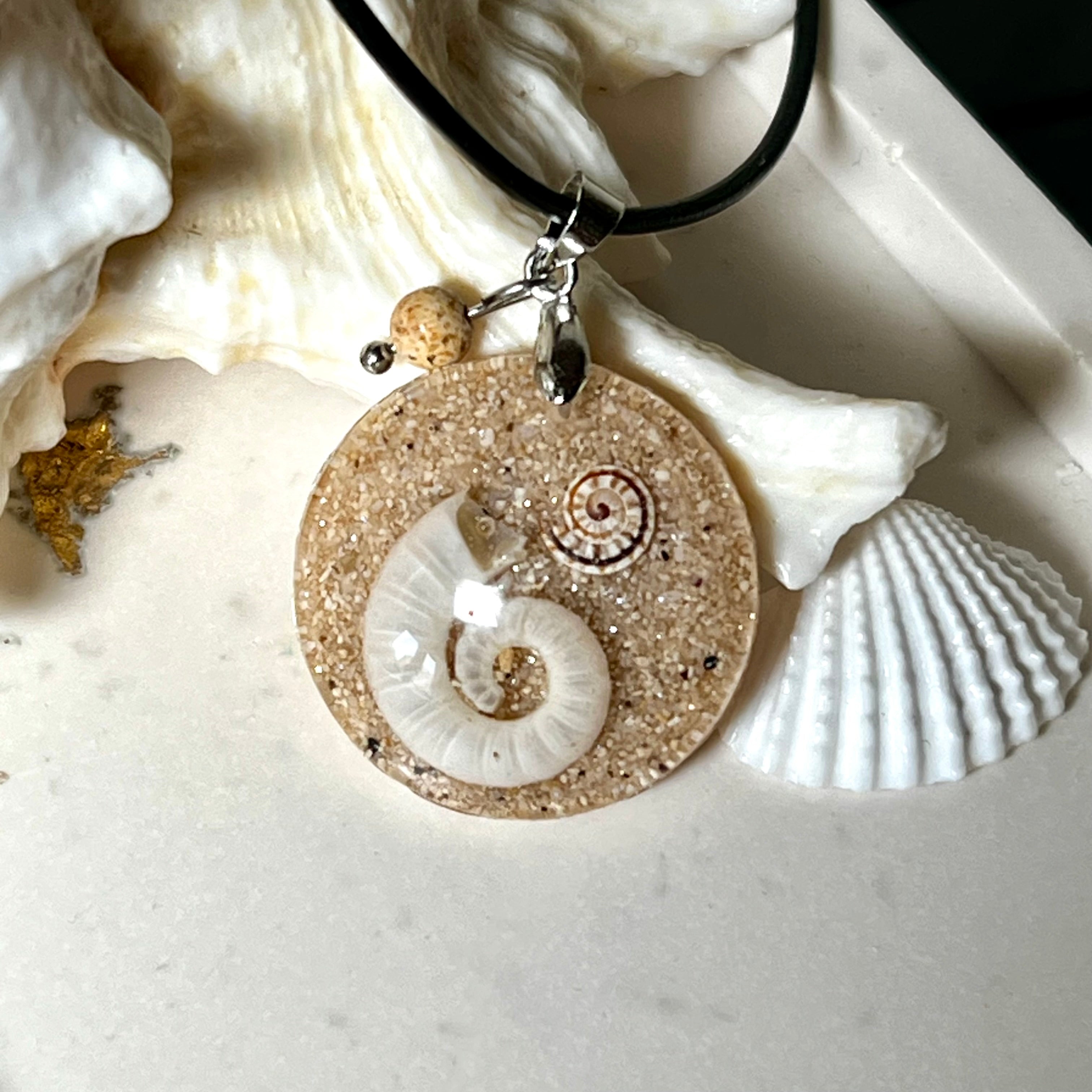 Handgemachter Anhänger mit echter Spirale, kleiner Schnecke, Meersand und feinem Glitzereffekt im Harz. Verziert mit einer Jaspisperle, Edelstahlöse und Lederkette mit Verlängerung. Maritimer Natur-Schmuck, inspiriert vom Ozean