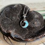 Feine Wellen-Kette aus rhodiniertem 925 Silber. Der runde Anhänger zeigt eine stilisierte Welle mit hellblauem Larimar-Cabochon, eingefasst in poliertem Silber. Größe des Anhängers ca. 23 x 13 mm, an einer 45 cm langen, 1 mm starken, rhodinierten Silberkette. 