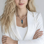 Rechteckiger Stabanhänger aus Maserholz und glasklarem Epoxidharz in tiefen Blau- und Türkistönen mit organischer Lagunen/Riff-Optik. Hochglanzpoliert, ca. 4,6 × 1,2 cm. Der Anhänger hängt an einer schwarzen Lederkette mit Edelstahl-Karabiner und 5-cm-Verlängerung (45 + 5 cm); die Anhängerschlaufe ist ebenfalls aus Edelstahl. Handgefertigtes Unikat, Lieferung in edler Schmuckbox – maritimer Look.