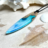 Surfbrett-Anhänger handgefertigt aus Maserholz & Harz in Blau-Weiß. Größe ca. 6,3 × 2 cm. Lederband verstellbar 26–47 cm, Schiebeknoten mit Holzperlen.