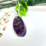 Ovaler Anhänger mit echter Pusteblume in Harz, Hintergrund Brombeerfarben. Größe 4 × 1,8 cm, versilberte Kette 50 cm mit Karabinerverschluss. Handgefertigtes Unikat.