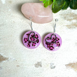 Handgemachte Leo-Creolen aus 925 Silber: Silber-Creolen 16 mm mit rosa Harz-Scheibe (2 cm) im Leoparden-Look und Edelstahl-Herzanhänger. Hängende Ohrringe in Animal-Print Stil, Gesamtlänge ca. 3,5 cm. Resin-Ohrringe für Alltag, Party oder Festival, femininer Statement-Schmuck in Rosa/Pink mit silberfarbenen Metallteilen. Einzeln gegossen, jedes Paar ein Unikat; leichte Abweichungen im Muster, Farbspiel und kleine Luftbläschen sind möglich und typisch für Handarbeit.