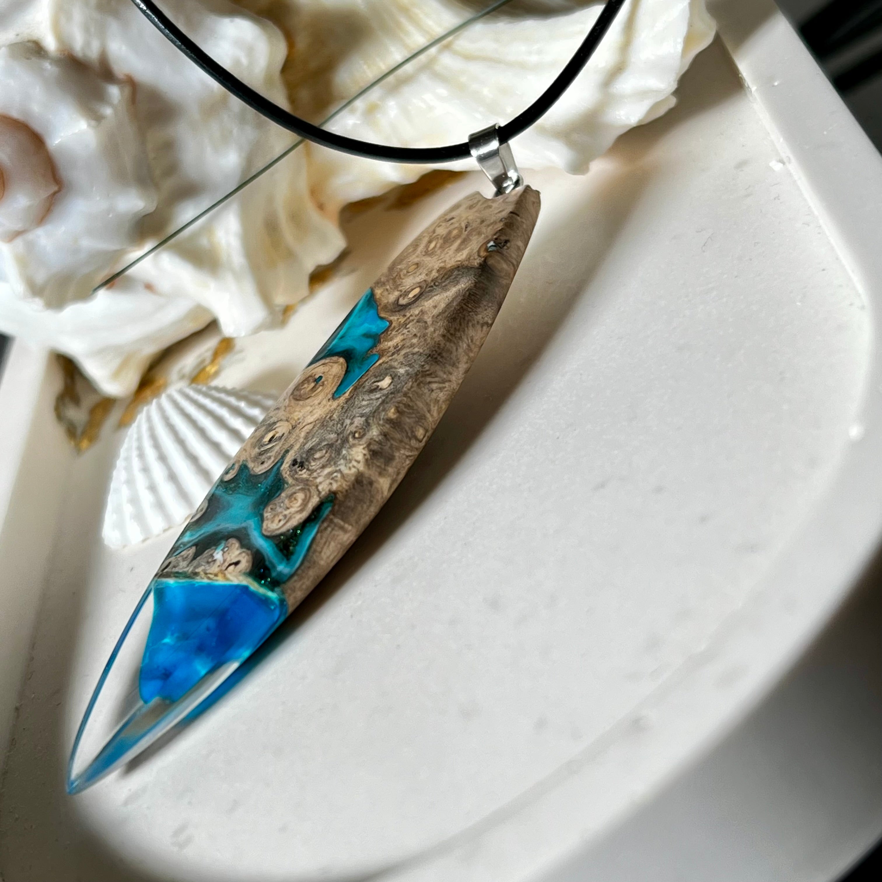 Handgefertigter Surfbrett-Anhänger aus Maserholz und transparentem Harz mit Farbverlauf in Blau und Weiß. Die natürliche Maserung des Holzes trifft auf ozeanartige Harzstrukturen. Größe ca. 6,7 x 2 cm, mit Edelstahlöse und Lederband inkl. Karabinerverschluss (45 cm + 5 cm Verlängerung). Jedes Stück ist ein Unikat – maritim, modern und mit viel Liebe gefertigt.