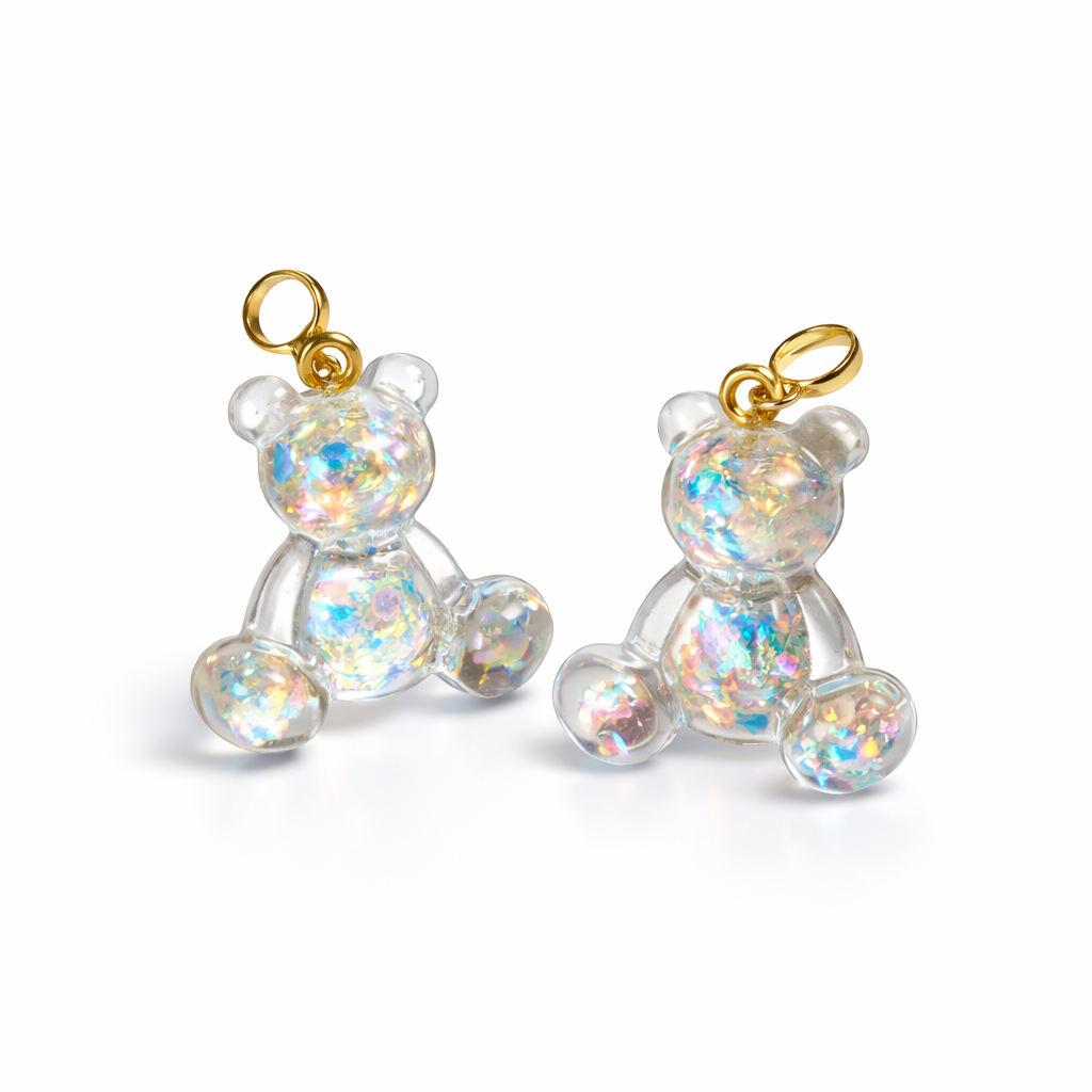 Kleiner Bärchen-Anhänger aus transparentem Harz mit irisierenden Flakes in Regenbogen-Schimmer, goldfarbene Anhängerschlaufe aus Edelstahl. Größe ca. 2,2 × 2,1 cm. Handgefertigtes Unikat; Flakes-Anordnung variiert, vereinzelt kleine Luftbläschen möglich.