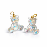 Kleiner Bärchen-Anhänger aus transparentem Harz mit irisierenden Flakes in Regenbogen-Schimmer, goldfarbene Anhängerschlaufe aus Edelstahl. Größe ca. 2,2 × 2,1 cm. Handgefertigtes Unikat; Flakes-Anordnung variiert, vereinzelt kleine Luftbläschen möglich.