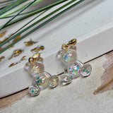 Kleiner Bärchen-Anhänger aus transparentem Harz mit irisierenden Flakes in Regenbogen-Schimmer, goldfarbene Anhängerschlaufe aus Edelstahl. Größe ca. 2,2 × 2,1 cm. Handgefertigtes Unikat; Flakes-Anordnung variiert, vereinzelt kleine Luftbläschen möglich.