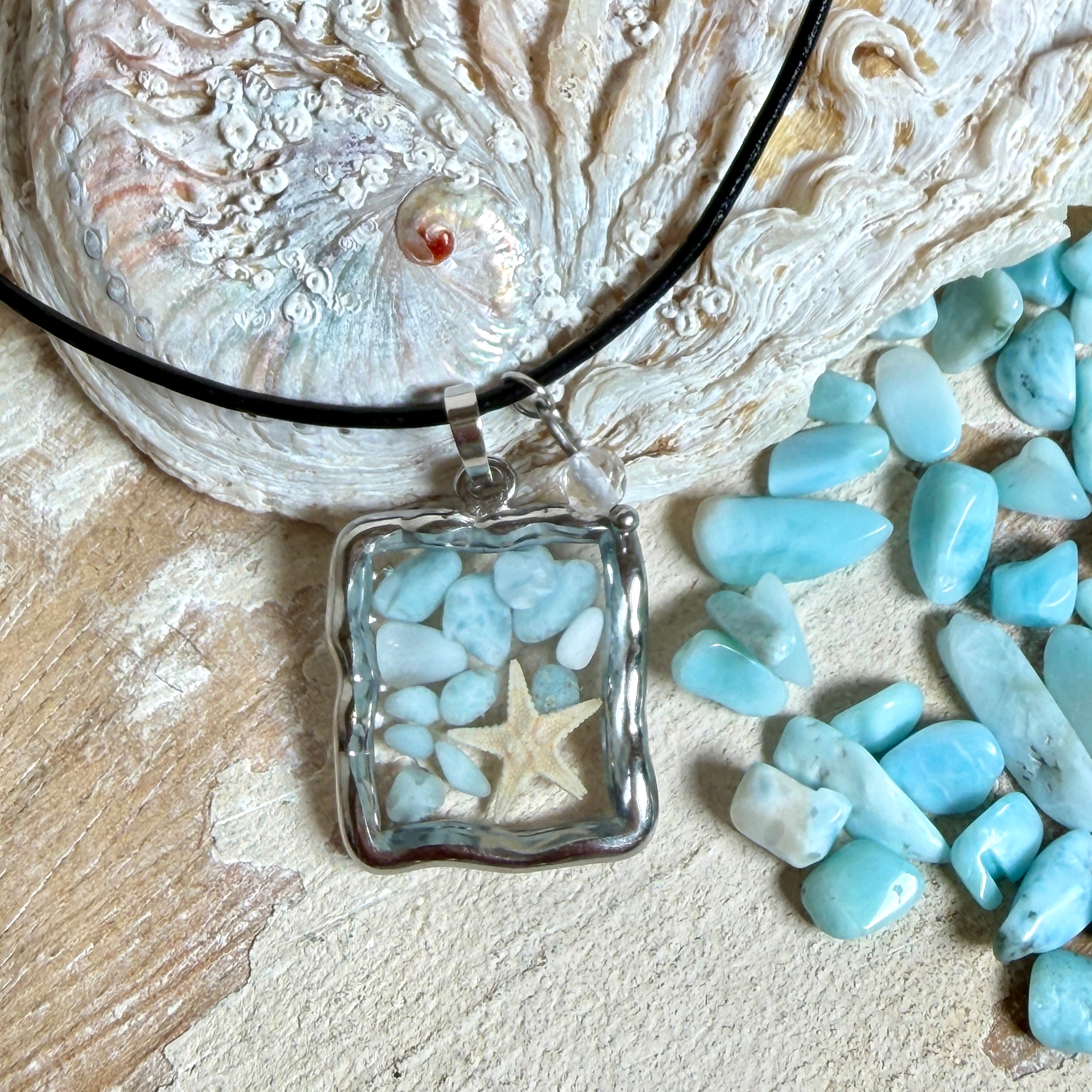 Quadratischer Larimar-Mosaik Anhänger im Edelstahlrahmen mit Seestern-Element und facettierter Bergkristall-Perle, eingebettet in Harz, an schwarzer Lederkette.