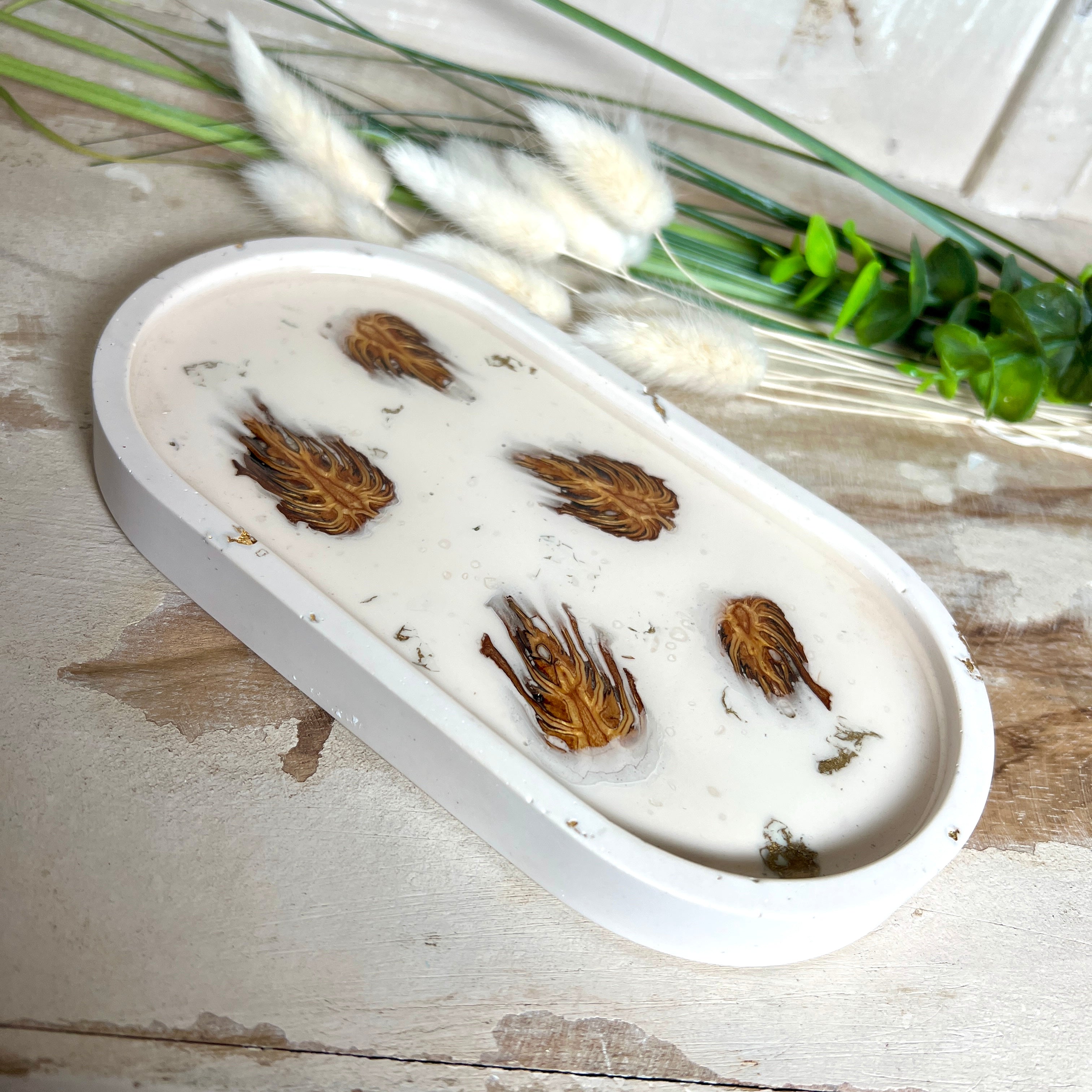 Handgefertigtes Schmucktablett aus Jesmonite mit echten Zapfen, die in einer glänzenden Resin-Schicht eingebettet sind. Die ovale Form und die natürliche Farbgebung machen es zu einem stilvollen Wohnaccessoire. Mit rutschfesten Korkpunkten auf der Unterseite ideal als Ablage für Schmuck, Schlüssel oder Dekoartikel. Jeder Artikel ist ein Unikat aus Handarbeit – Lieferung ohne Dekoration.