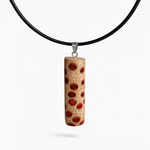 Handgefertigter Halsanhänger aus echtem Banksiazapfen, veredelt mit rotem Harz in den natürlichen Kammern; ca. 5,5 × 1,6 cm. Mit Anhängerschlaufe aus Edelstahl an schwarzer Lederkette (45 cm + 5 cm Verlängerung) mit Edelstahl-Karabiner. Detailaufnahme bzw. Tragebild vor neutralem, natürlichem Hintergrund.