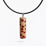 Handgefertigter Halsanhänger aus echtem Banksiazapfen, veredelt mit rotem Harz in den natürlichen Kammern; ca. 5,5 × 1,6 cm. Mit Anhängerschlaufe aus Edelstahl an schwarzer Lederkette (45 cm + 5 cm Verlängerung) mit Edelstahl-Karabiner. Detailaufnahme bzw. Tragebild vor neutralem, natürlichem Hintergrund.