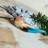 Handgefertigter Anhänger aus Edelholz und transparent-türkisblauem Epoxidharz, glatt poliert. Größe ca. 6,7 × 2,0 cm. Mit Edelstahlöse an schwarzer Lederkette (45 cm + 5 cm Edelstahl-Verlängerung, Karabiner). Maritimer, moderner Unisex-Schmuck mit natürlicher Holzmaserung; kleine Lufteinschlüsse sind charakteristisch.